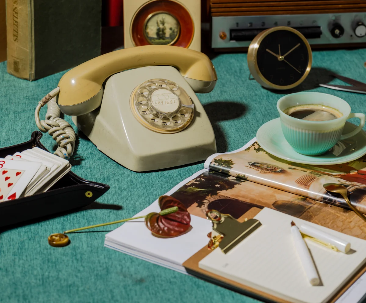 Cream rotary phone in a styled flat-lay with playing cards, coffee, and a small clock